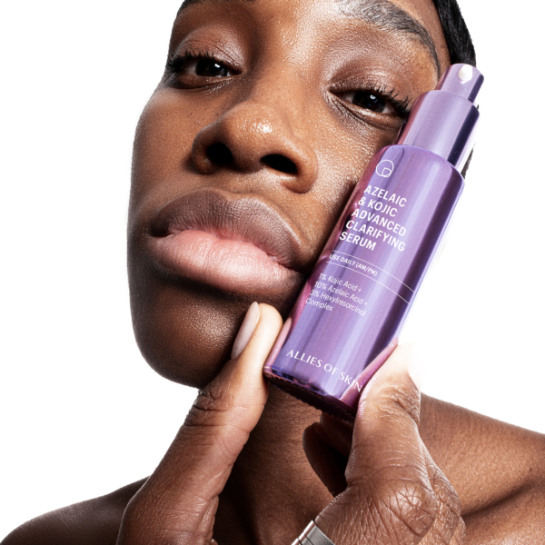 Woman holding Allies Of Skin Azelaic And Kojic Advanced Clarifying Serum near face to highlight brightening and clarifying benefits