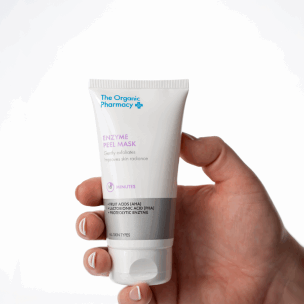 Hand holding The Organic Pharmacy Enzyme Peel Mask 60ml jar, formulated to gently exfoliate and brighten the skin