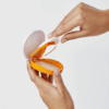 Hand opening a Heliocare 360 Oil-Free Compact SPF sunscreen makeup compact, showing the product packaging and applicator inside.