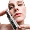 Woman holding Allies Of Skin Tranexamic And Arbutin Advanced Brightening Serum 30ml close to her face, showcasing the product