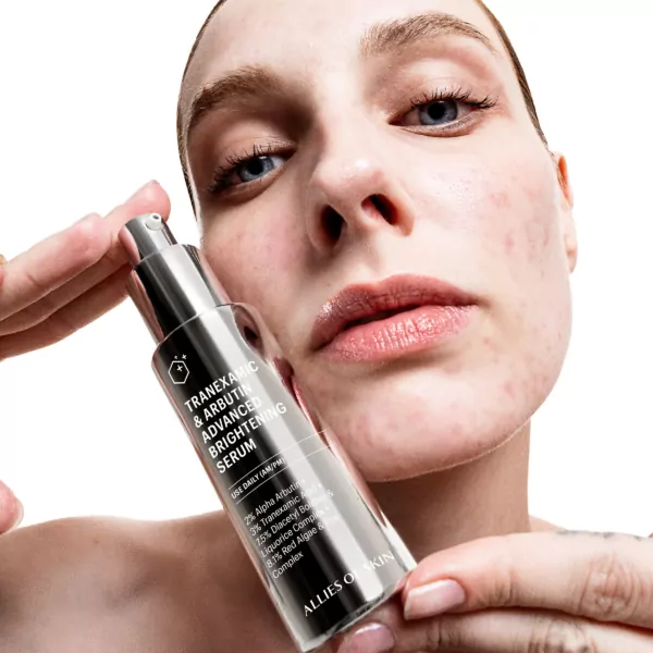Woman holding Allies Of Skin Tranexamic And Arbutin Advanced Brightening Serum 30ml close to her face, showcasing the product